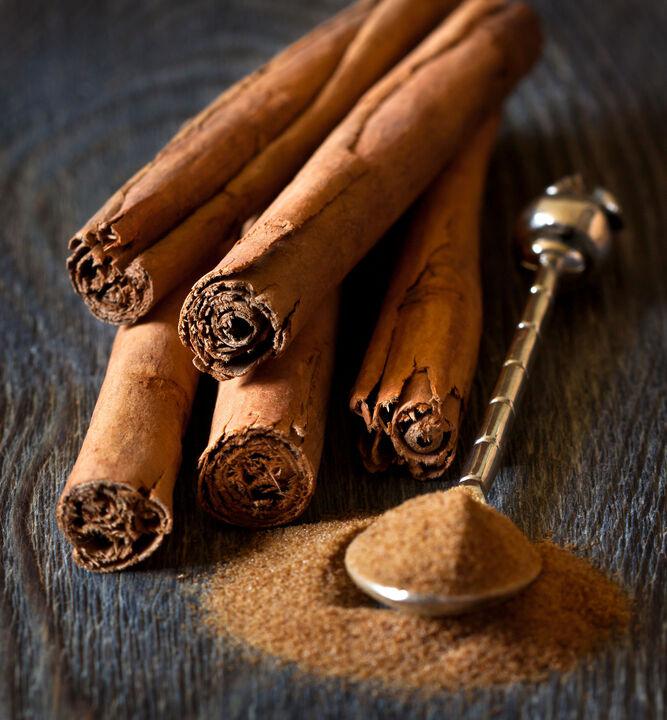 Primer plano de la canela de Ceilán sobre una mesa de madera. A su lado, a la derecha, se encuentra una elegante cuchara sobre un pequeño montón de canela de Ceilán molida. La cuchara también contiene parte de la canela.